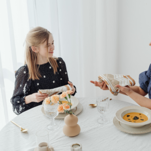 Etiquette teacher teaching table manners and napkin etiquette to a child at the dining table